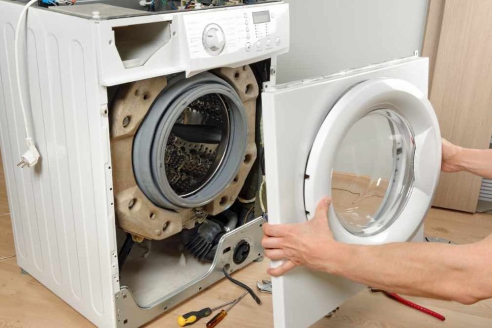 A man repairs a washing machine with the door ajar, highlighting a laundry appliance service based in Reno, NV.