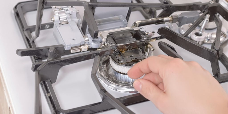 A person repairs a stove top, using a metal component to ensure proper functionality and safety.