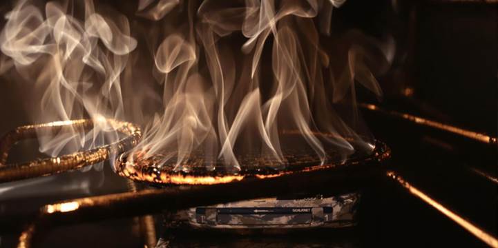 A pan of food ablaze inside an oven, flames visible, highlighting a cooking mishap.
